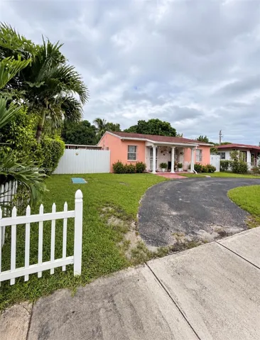 Stucco exterior featuring a covered front porch with decorative columns, a paved curved driveway, and white picket fencing