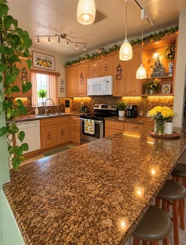 Kitchen featuring stone countertops, custom wood cabinetry, stainless steel appliances, tiered pendant lighting, and under-cabinet illumination