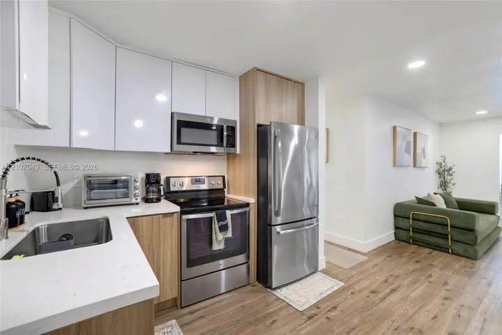 Kitchen featuring white upper cabinetry, wood-finish lower cabinetry, quartz countertops, stainless steel appliances, and wood-finish flooring