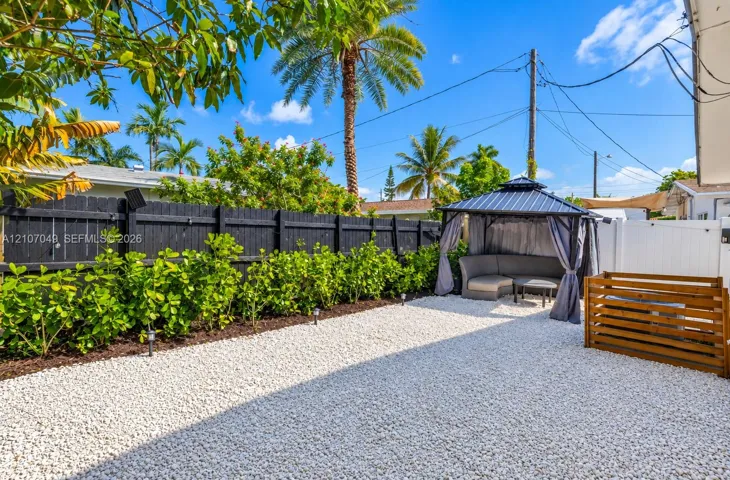 Backyard featuring a white stone-covered ground, black-painted wood privacy fencing, a manicured hedge border, and a wood-slat enclosure