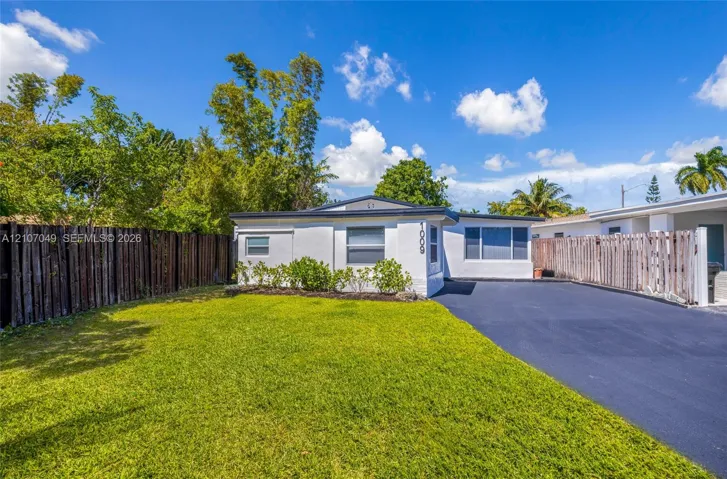 Single-story residence featuring a white stucco exterior, asphalt driveway, horizontal wood fencing, and manicured lawn