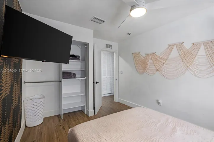 Wood-finish flooring, accent wall with patterned wall covering, built-in open shelving, and a ceiling-mounted light fixture with integrated fan