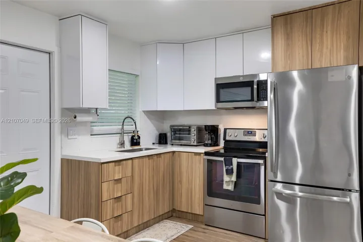 Two-tone cabinetry featuring white upper and wood-finish lower cabinets, stainless steel appliances, white solid-surface countertops, and an undermount sink with a pull-down faucet