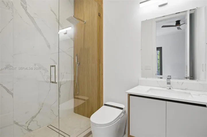 Walk-in shower with floor-to-ceiling stone-patterned tile, vertical wood-slat accent wall, rainfall showerhead, glass enclosure, and floating vanity with integrated countertop and sink