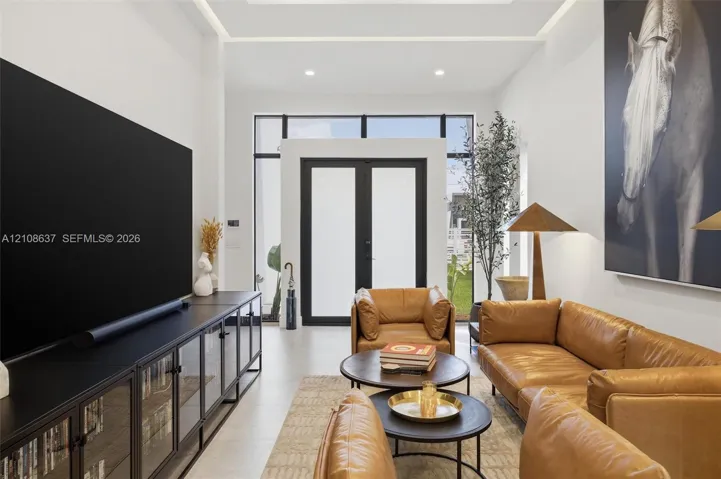 Living space featuring high ceilings with recessed perimeter lighting, large-format tile flooring, and floor-to-ceiling black-framed glass double doors