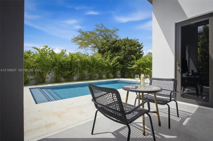 Private swimming pool with integrated stairs, expansive light-toned stone decking, and tall perimeter privacy landscaping