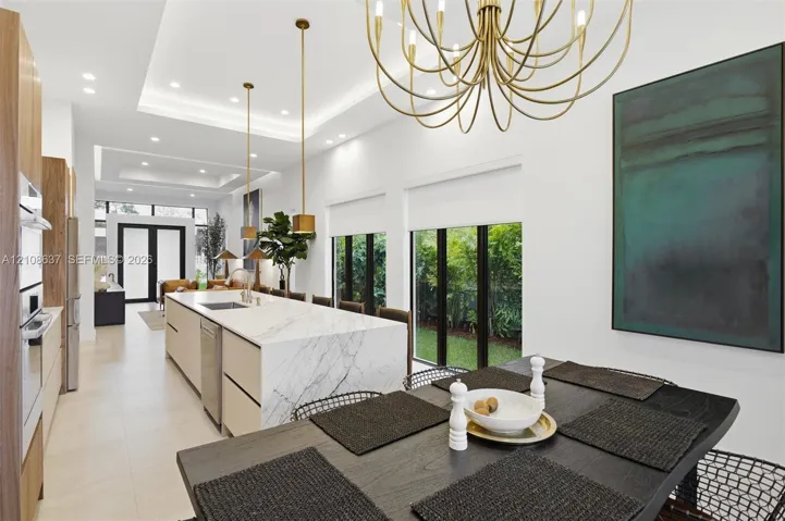 Kitchen featuring a waterfall island with stone-finish countertops, ceiling-recessed tray lighting, custom flat-panel cabinetry, metallic pendant lighting, and floor-to-ceiling windows