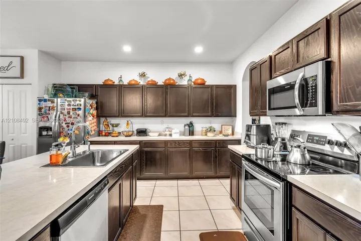 Kitchen featuring dark wood cabinetry, stainless steel appliances, solid surface countertops, a stainless steel undermount sink, and tiled flooring