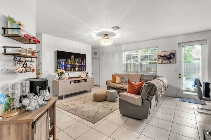 Living area featuring tile flooring, a multi-tiered crystal-style chandelier, horizontal window blinds, and a glass-paneled exterior door