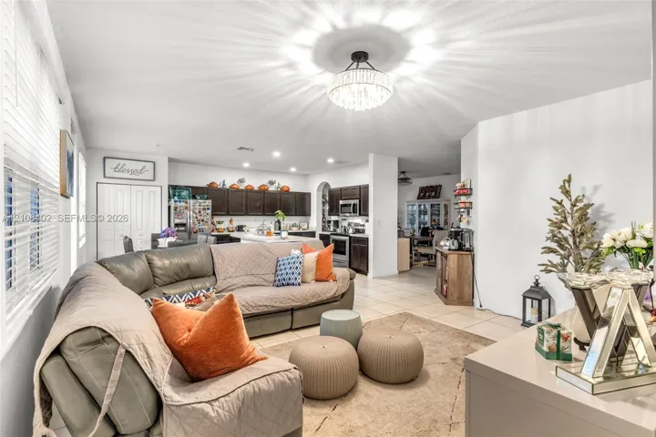 Open-concept interior featuring large-format tile flooring, a central drum-style chandelier with tiered crystals, dark-toned cabinetry, and recessed lighting