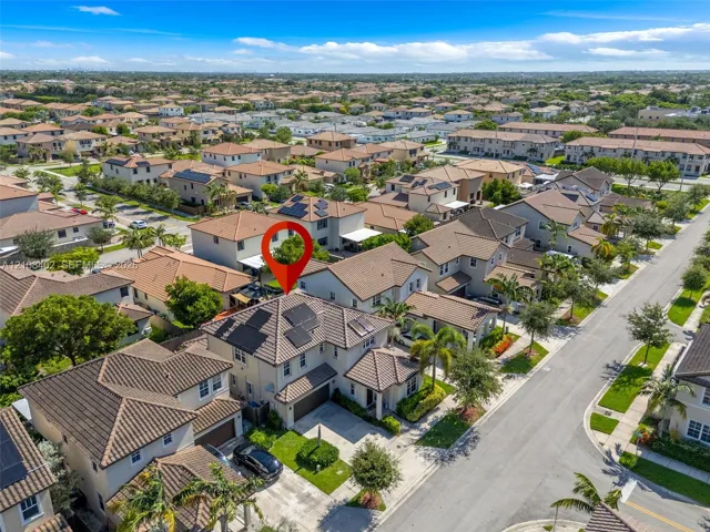Aerial view of two-story residence featuring a tile roof, installed solar panels, attached garage, and paved driveway within a planned community