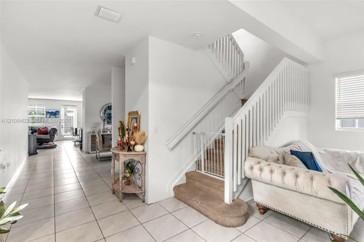 Staircase featuring white balusters and a carpeted tread, complemented by neutral-toned floor tile throughout