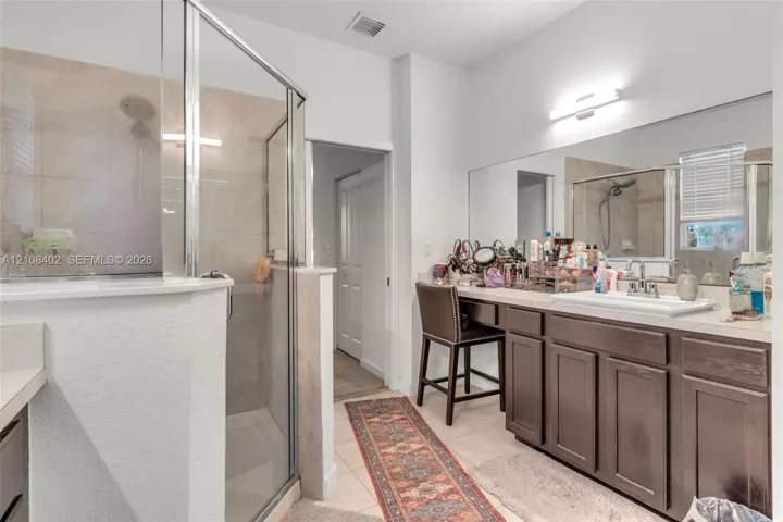 Bathroom featuring a walk-in shower with glass enclosure, dark-stained cabinetry, light-toned countertop with an integrated sink, and a full-width vanity mirror with integrated lighting