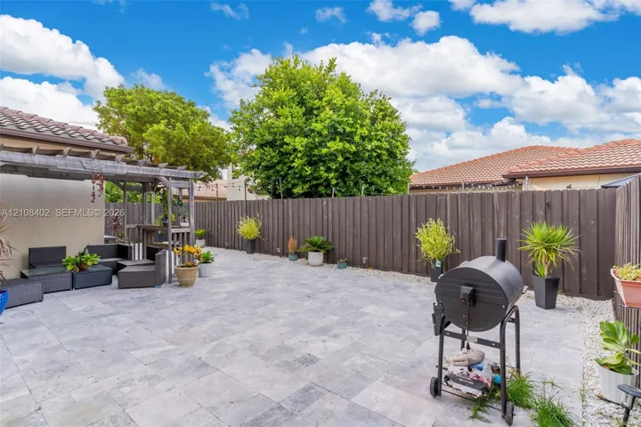 Outdoor living area featuring a neutral-toned stone paver patio, a wooden pergola, and a full-height privacy fence