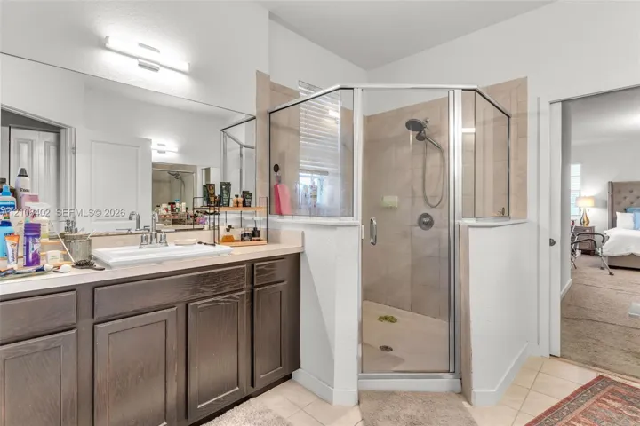 Bathroom featuring dark wood-finish cabinetry, a rectangular sink with a chrome faucet, a large wall-mounted mirror, and a corner shower enclosure with tile wall surround