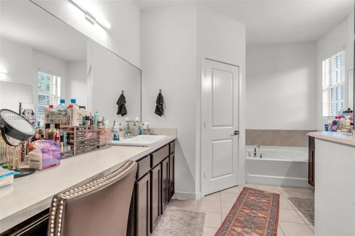 Bathroom featuring an expansive vanity with dark-finish cabinetry, a large wall-to-wall mirror, a rectangular drop-in sink, and a separate soaking tub with tiled surround