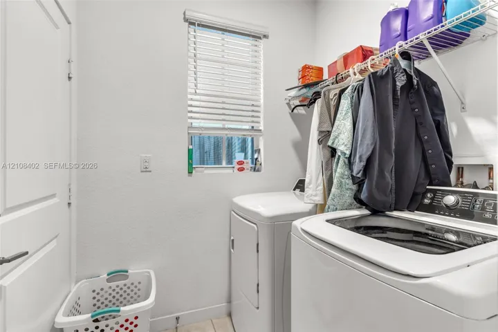 Laundry space featuring a window with horizontal blinds, wall-mounted wire shelving, and neutral wall finish