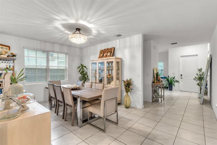 Open-concept dining area featuring large-format ceramic tile flooring, a tiered crystal drum chandelier, and a recessed window with horizontal blinds
