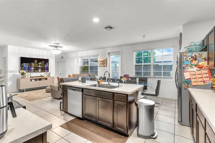 Kitchen featuring a central island with a stainless steel undermount sink, dark wood-finish cabinetry, solid-surface countertops, tile flooring, and stainless steel appliances