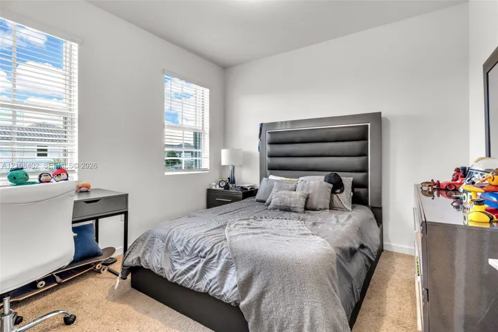 Neutral-toned bedroom featuring plush carpeting, dual-pane windows with horizontal blinds, and smooth-finish white walls