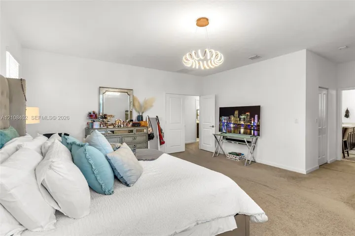 Neutral-toned wall-to-wall carpeting, modern circular spiral-design chandelier, two-panel interior doors, and crisp white wall finish