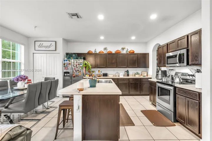 Kitchen featuring dark-finish wood cabinetry, a central island with a solid surface countertop, tile flooring, and stainless steel appliances
