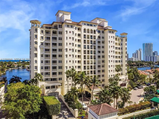 Mid-rise waterfront high-rise building featuring multi-level balconies, arched architectural detailing, a clay tile roof, and porte-cochère entry