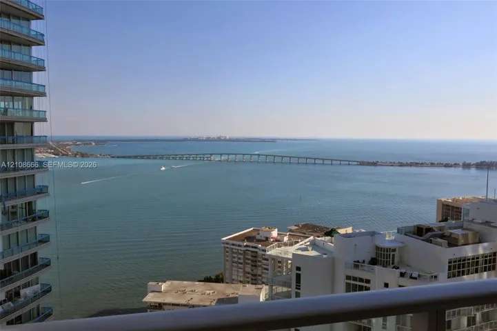Elevated balcony with a horizontal metal railing overlooking a maritime horizon, bridge, and coastal cityscape