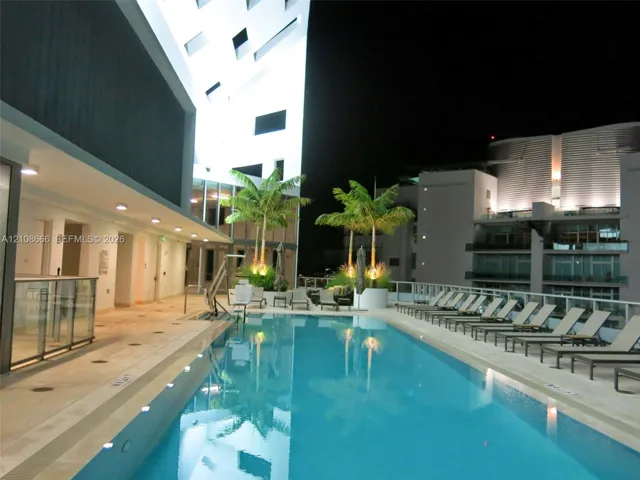 Rectangular swimming pool featuring a light-toned deck, integrated pool lift, recessed lighting, and palm tree planters