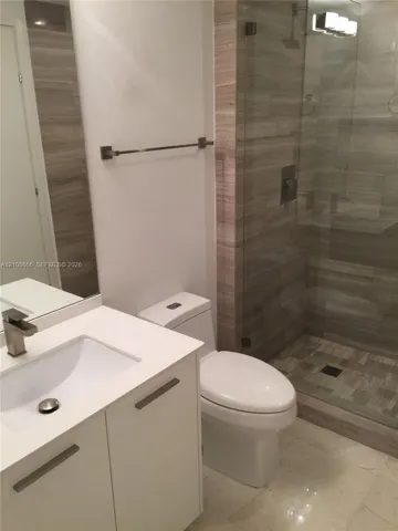 Modern bathroom featuring a white vanity with a rectangular basin, metallic single-handle faucet, glass-enclosed shower with tiled surround, and integrated lighting