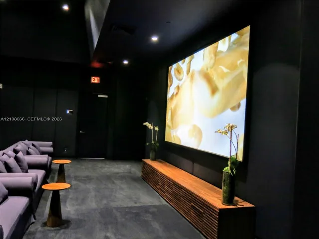 Media room featuring dark wall finishes, a large-format mounted screen, and a custom slatted wood-finish media console with recessed ceiling lighting