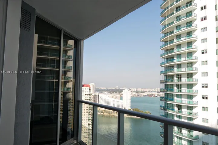 Private balcony with a metal and glass railing, floor-to-ceiling glass sliding door, and urban and water scenery