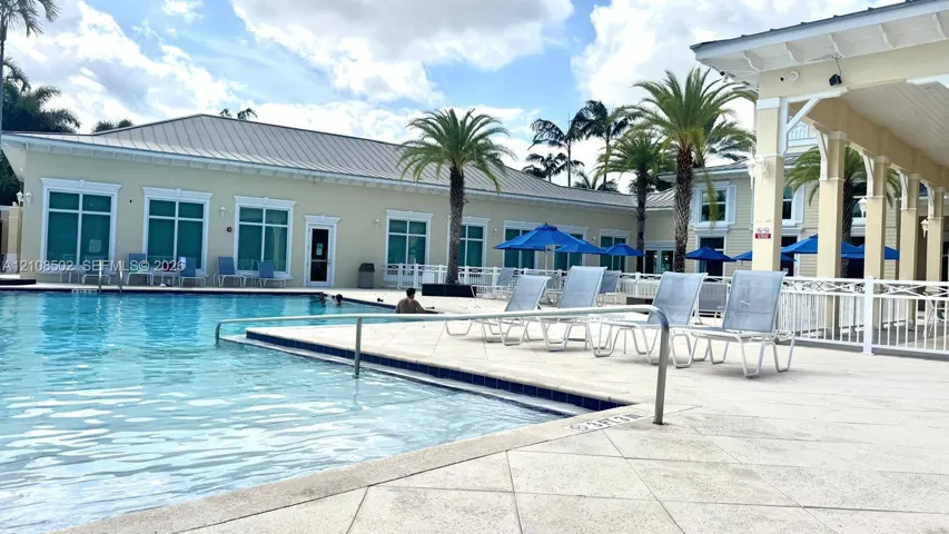 Swimming pool with a paved deck, metal perimeter fencing, and a covered pavilion structure