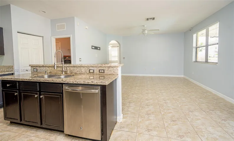 Kitchen featuring dark cabinetry, stone-finish countertops, stainless steel dual-basin sink with pull-down faucet, stainless steel dishwasher, and ceramic tile flooring