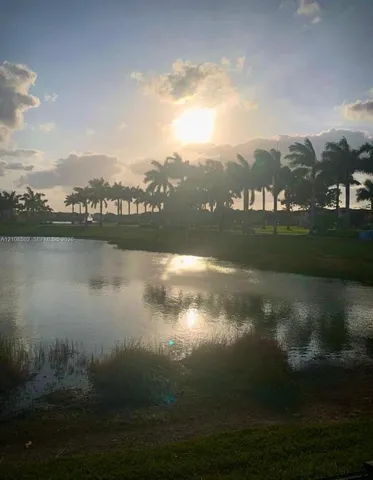 Waterfront property featuring a lake, manicured grass landscape, and mature palm trees