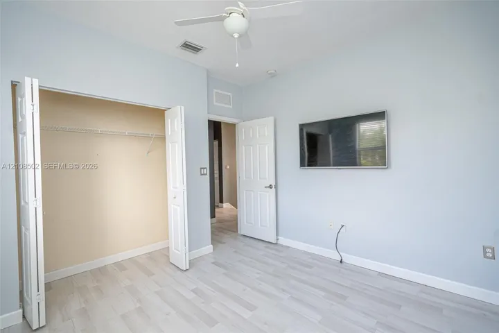 Room featuring wood-finish flooring, a ceiling fan with integrated lighting, and a closet with bifold doors
