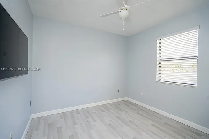 Neutral wall-toned room featuring wood-finish flooring, a white ceiling fan, and a window with horizontal blinds