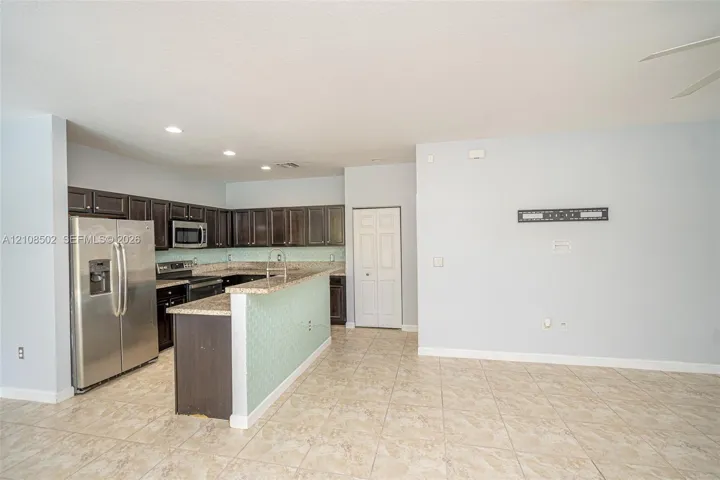 Kitchen featuring dark wood cabinetry, stainless steel appliances, speckled stone-finish countertops, mosaic-tiled breakfast bar, and tile flooring