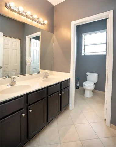 Dual vanity featuring dark cabinetry, solid surface countertop, integrated dual sinks, and large wall-mounted mirror