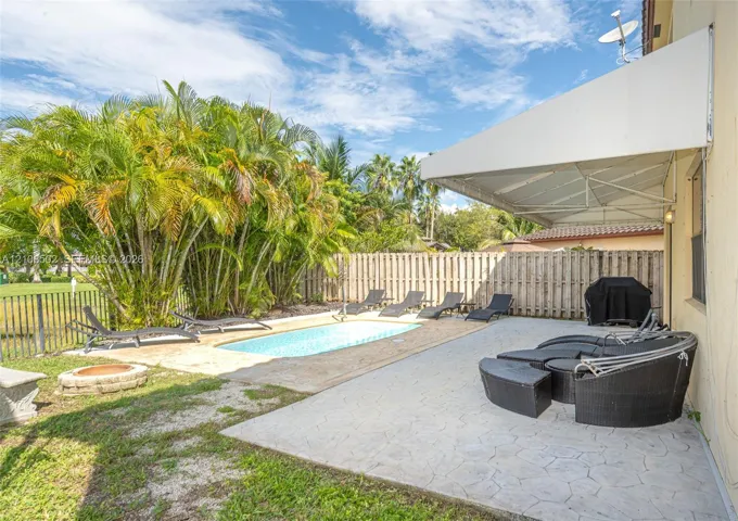 Backyard featuring a concrete-paver patio, retractable fabric awning, in-ground swimming pool, stone-finish fire pit, and wood-style privacy fencing