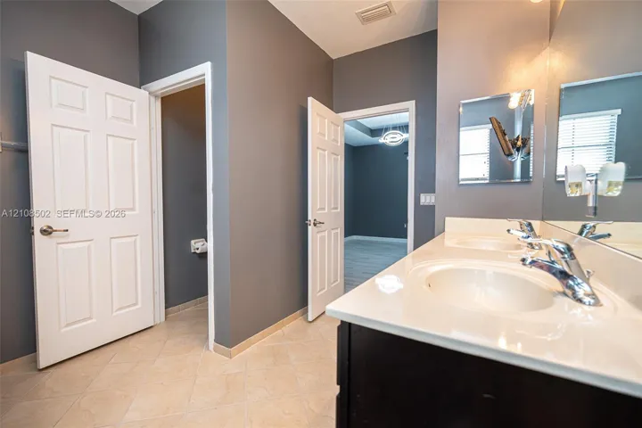 Vanity featuring a solid-surface countertop with dual integrated sinks, polished chrome fixtures, and a large-format wall mirror