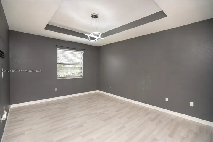 Tray ceiling featuring a contemporary circular chandelier, light-toned wood-finish flooring, and single-pane window with installed blinds