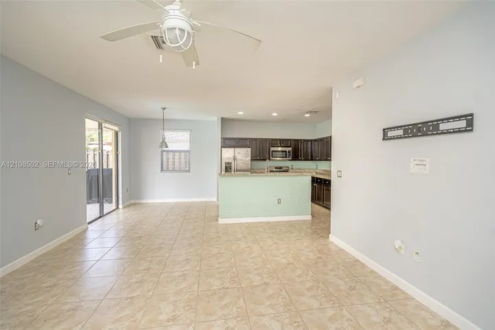 Open-concept interior featuring tile flooring, a kitchen peninsula with a tiled front, dark-finish cabinetry, built-in stainless steel appliances, and a ceiling fan with integrated lighting