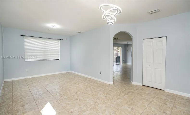 Interior space featuring tile flooring, modern sculptural LED chandelier, arched entryway, and double-door closet