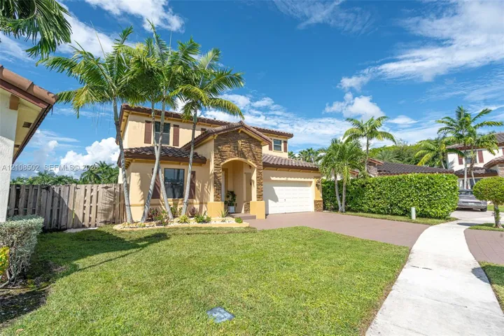 Two-story exterior featuring a stone veneer facade, a tiled roof, a paved driveway, and palm tree landscaping