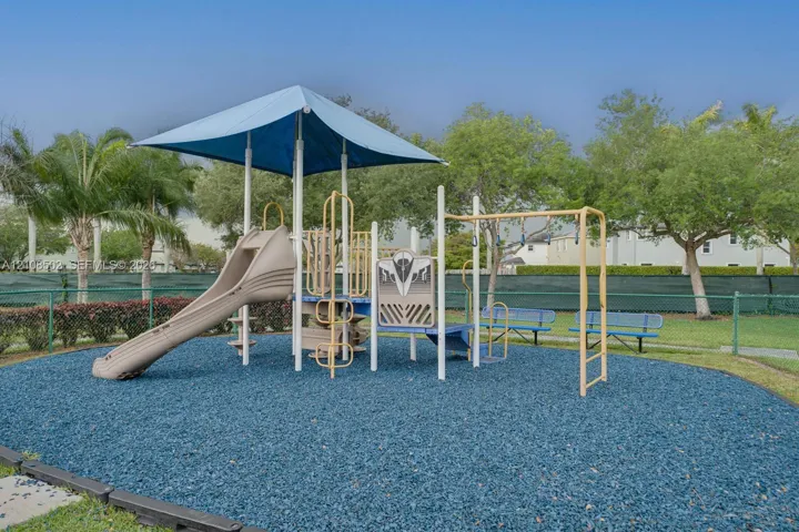 Outdoor recreation area featuring a structured play system with a canopy, integrated slide, and built-in bench seating, all set within a landscaped perimeter