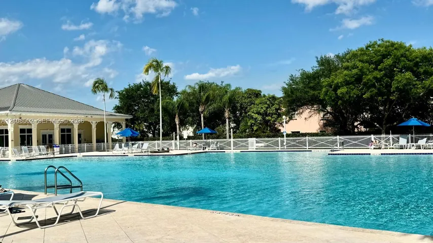 Large swimming pool with concrete decking, perimeter fencing, and an adjacent structure featuring covered patio space