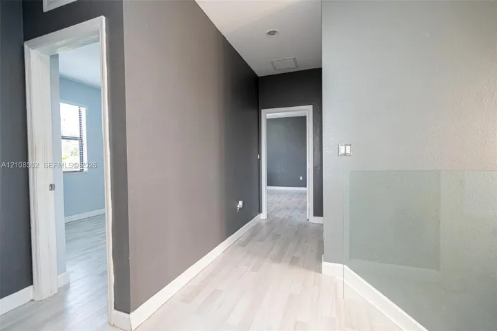 Interior hall featuring wood-finish flooring, two-toned wall paint, recessed lighting, and a minimalist glass panel railing