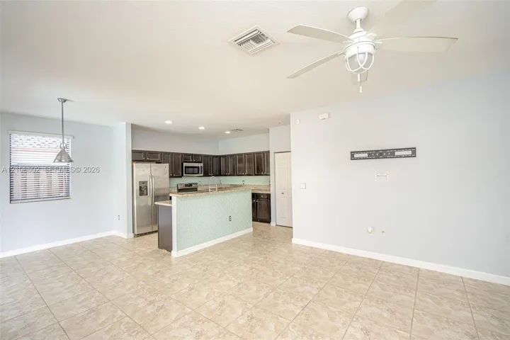 Open-concept floor plan featuring tile flooring, dark wood-finish cabinetry, stainless steel appliances, a peninsula counter, and a ceiling fan with integrated lighting