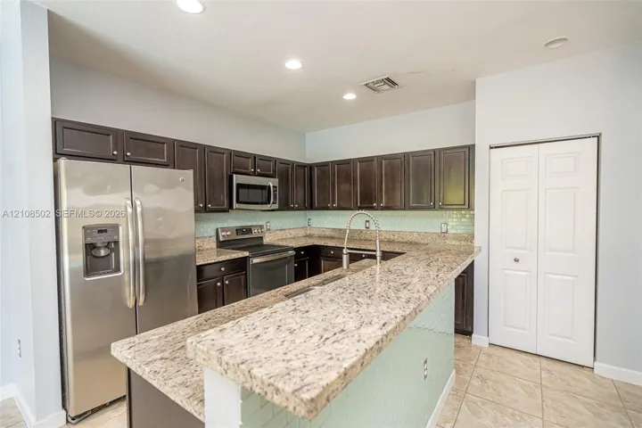 Kitchen featuring dark cabinetry, stone-finish countertops, subway tile backsplash, stainless steel appliances, and tile flooring